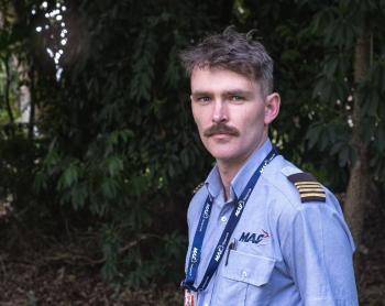 A pilot standing in the shade of a tree looking into camera