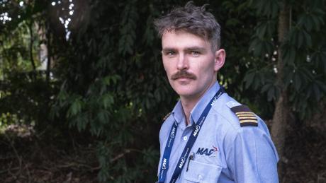 A pilot standing in the shade of a tree looking into camera