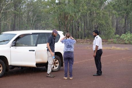 Pilits and nurse standing at car beside dirt airstrip